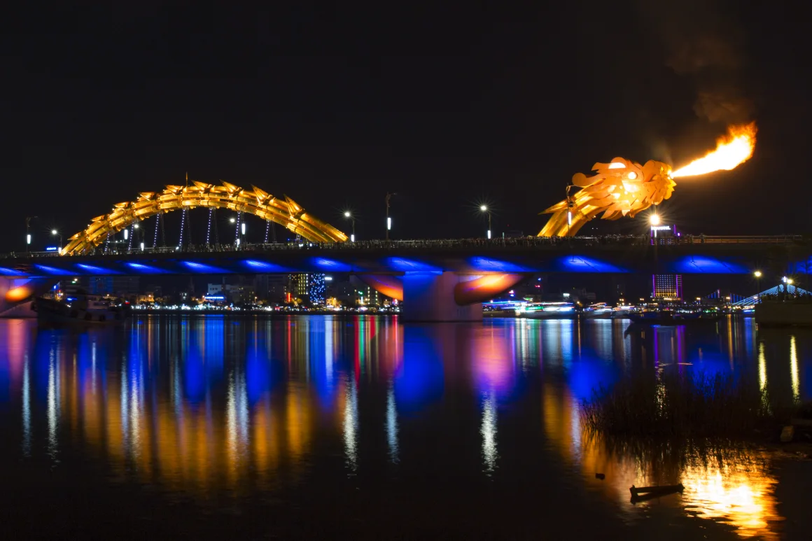 Dragon Bridge Da Nang breathing fire at night, reflected in the Han River