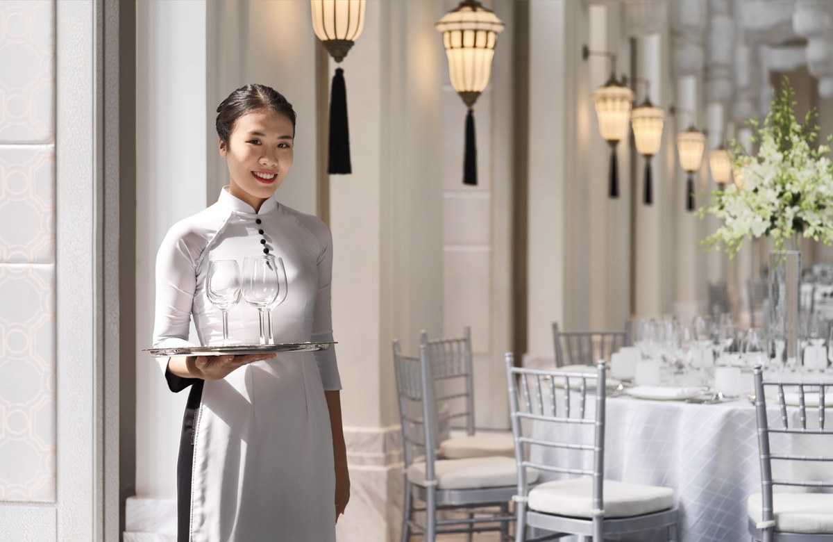 InterContinental Danang service staff in ao dai carrying wine glasses through dining room