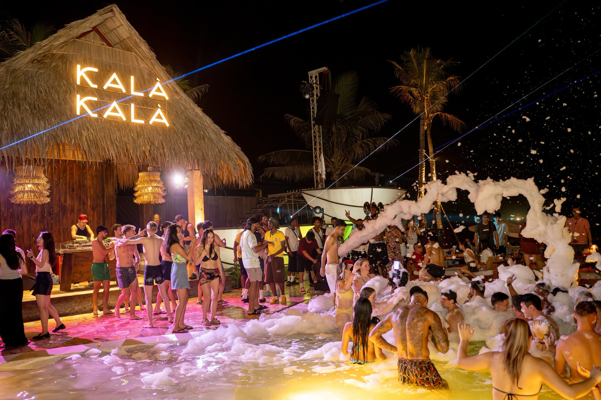 Kal&agrave; Kal&agrave; Beach Club Da Nang, foam party beach night, packed crowd dancing on the sand, neon Kal&agrave; Kal&agrave; sign on thatched beach hut