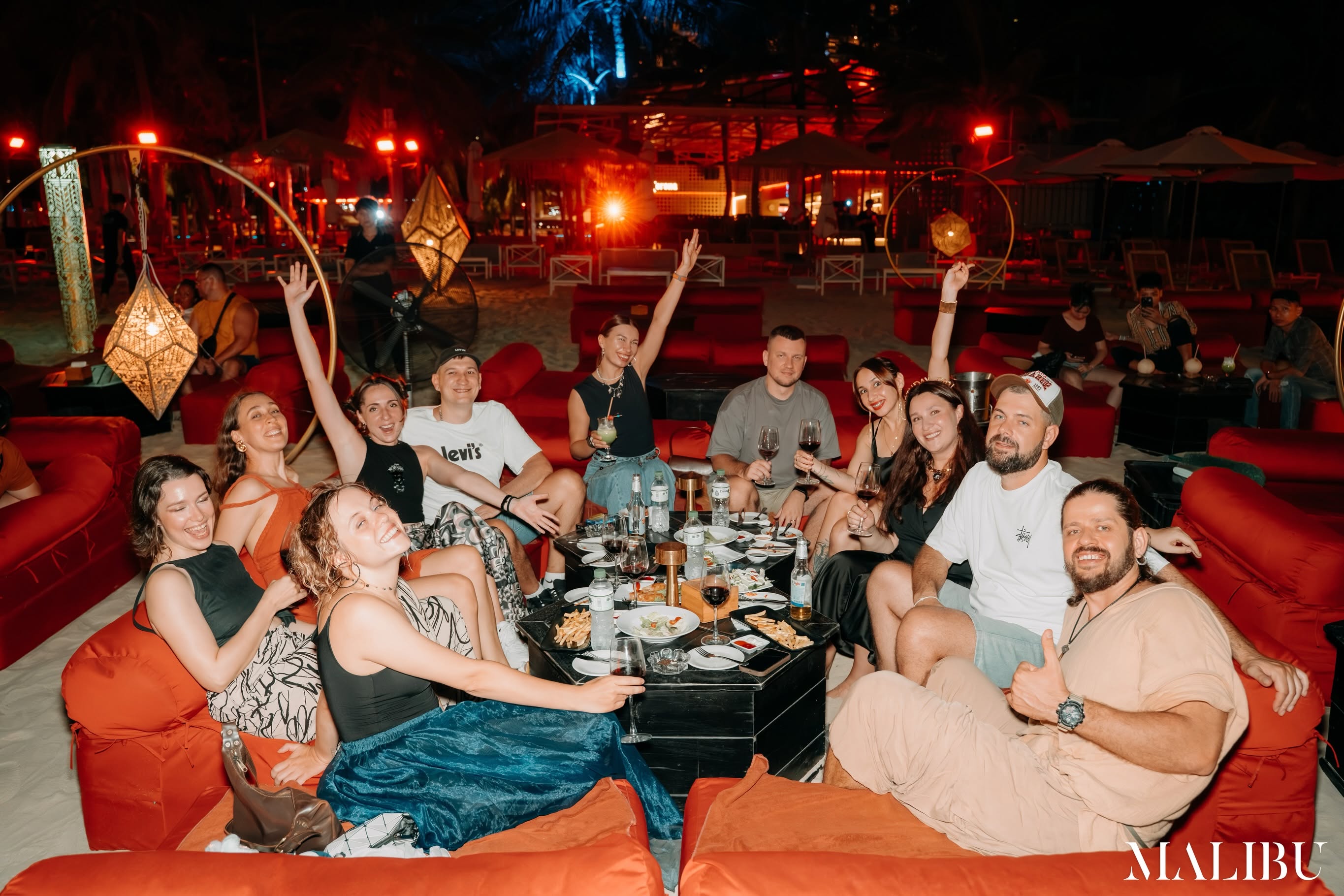 Malibu Beach Club Da Nang, guests on red cushions on the beach at night
